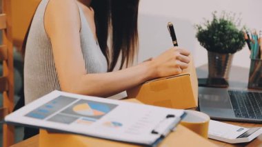 Genç Asyalı kadın dizüstü bilgisayar kullanıyor ve not defterine kalemle ve hesap makinesiyle yazıyor evde, iş ve mali muhasebe kavramında