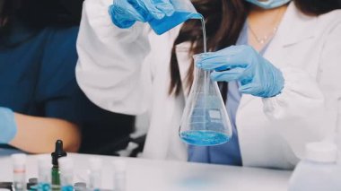 Kadın laboratuvar teknisyeni elinde mavi sıvı tüpü tutuyor.