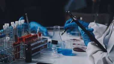 Koruyucu eldivenli laboratuar asistanı elinde bir şişe ve test tüpü tutuyor.