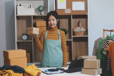 Vlogger, blog yazarı, küçük KOBİ iş kadını güzel bir kadın cep telefonuyla kıyafetleri satıyor canlı yayın satışı yapıyor, ana ofiste ürün sunumu detaylarını gösteriyor, girişimci ekommerce