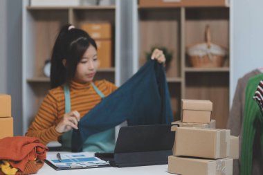 Vlogger, blog yazarı, küçük KOBİ iş kadını güzel bir kadın cep telefonuyla kıyafetleri satıyor canlı yayın satışı yapıyor, ana ofiste ürün sunumu detaylarını gösteriyor, girişimci ekommerce