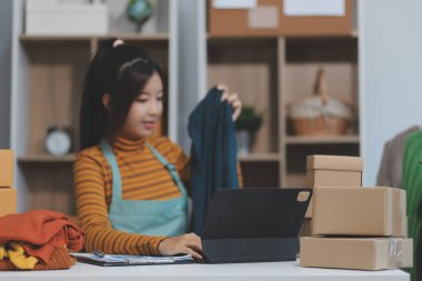 Vlogger, blog yazarı, küçük KOBİ iş kadını güzel bir kadın cep telefonuyla kıyafetleri satıyor canlı yayın satışı yapıyor, ana ofiste ürün sunumu detaylarını gösteriyor, girişimci ekommerce