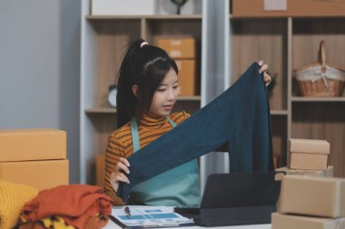 Vlogger, blog yazarı, küçük KOBİ iş kadını güzel bir kadın cep telefonuyla kıyafetleri satıyor canlı yayın satışı yapıyor, ana ofiste ürün sunumu detaylarını gösteriyor, girişimci ekommerce