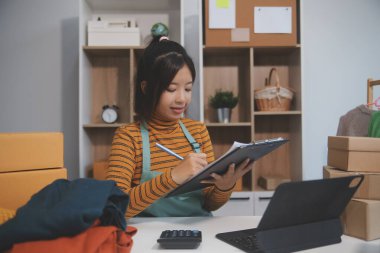 Vlogger, blog yazarı, küçük KOBİ iş kadını güzel bir kadın cep telefonuyla kıyafetleri satıyor canlı yayın satışı yapıyor, ana ofiste ürün sunumu detaylarını gösteriyor, girişimci ekommerce