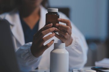 Doktor ilaç şişesini tutuyor ve ofiste notlar alıyor..