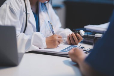 Ofiste çalışan ve hastayı dinleyen doktor semptomlarını, sağlık hizmetlerini ve yardım kavramlarını açıklıyor.