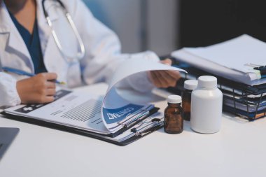 Doktor masasında oturuyor ve hastası için reçete yazıyor.