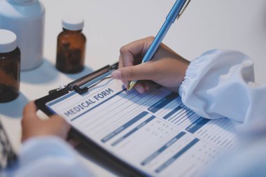 Doktor masasında oturuyor ve hastası için reçete yazıyor.