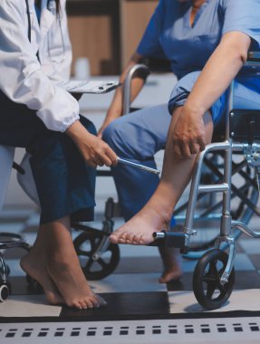 Asyalı, genç, profesyonel, dost canlısı mavi hastane üniformalı kadın hemşire yaşlı, yaşlı, sağlıksız, dört bacaklı, yürüyen bir hastanın fiziksel terapisine yardım ediyor..