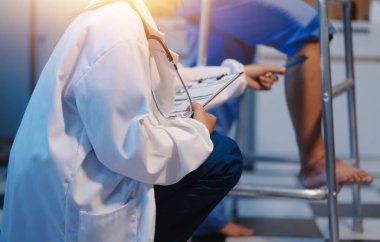 Asyalı, genç, profesyonel, dost canlısı mavi hastane üniformalı kadın hemşire yaşlı, yaşlı, sağlıksız, dört bacaklı, yürüyen bir hastanın fiziksel terapisine yardım ediyor..