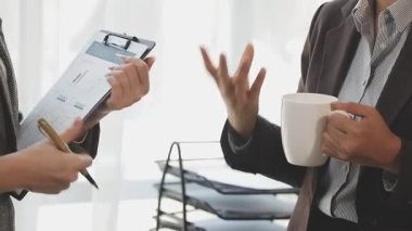 Elinde kahve fincanı olan bir iş adamı ofisteki meslektaşını işaret ediyor..
