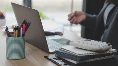 Ofisteki ahşap masaya dizüstü bilgisayar, kalem ve not defteri tutan bir kadının elini kapat..