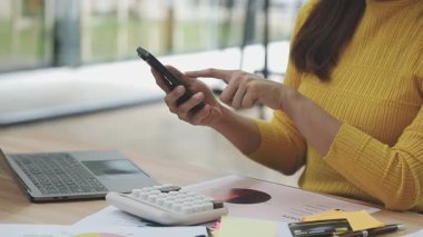 Genç Asyalı kadın evde akıllı telefon ve dizüstü bilgisayarla çalışıyor..