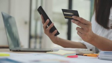 Kredi kartı tutan ve online alışveriş için laptop kullanan genç bir kadın.