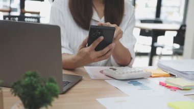 Genç Asyalı iş kadını ofiste dizüstü bilgisayar ve akıllı telefon kullanıyor..