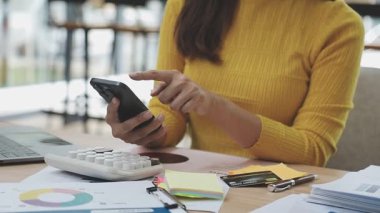 Ofis masasında akıllı telefon ve hesap makinesi tutan genç bir kadın..