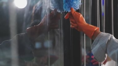 Eldivenli kadın pencereyi paçavrayla temizliyor.