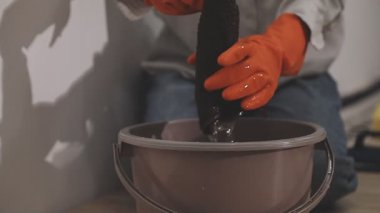 Beyaz gömlekli ve siyah eldivenli bir adam kova dolusu su tutuyor..