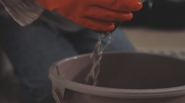 Eldivenli bir adamın elinde su damlasıyla kovayı tutmasını yakından izle..