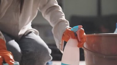 Mavi eldivenli, beyaz gömlekli, fırçalı ve paçavralı bir kadın.