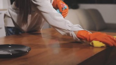 Kadın odada bez parçasıyla masayı temizliyor.