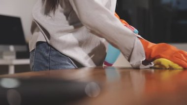 Yakın plan. Sarı önlüklü kadın elinde bez parçasıyla mutfak masasını tutuyor ve yerleri temizliyor.