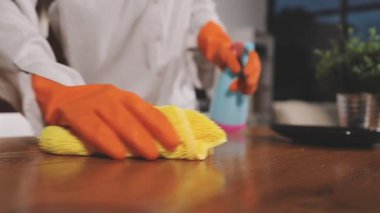 Eldivenli bir kadın, bir bez ve bir şişeyle masasını temizliyor.