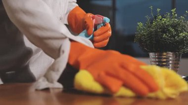 Masasında bez parçası ve sprey şişesi olan lastik eldivenli genç bir adam.