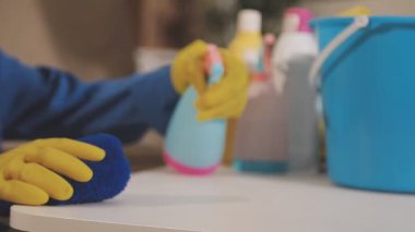 Sarı eldivenli genç bir adam ahşap bir masayı paçavrayla temizliyor..