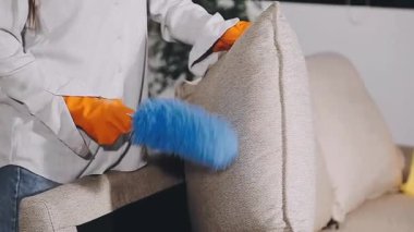 Kadın oturma odasında fırçayla kanepeyi temizliyor.