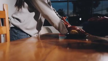 Genç bir kadın mutfakta bir bez ve sprey şişeyle masayı temizliyor..