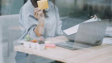 Ofiste dizüstü bilgisayarıyla çalışan genç bir kadın, bir dizüstü bilgisayar üzerinde çalışıyor ve elinde bir kahve fincanı tutuyor..