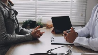 Doktor ofisinde otururken hastasıyla konuşuyor.