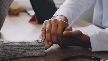 Steteskoplu erkek hastanın tıbbi klinikteki Afrikalı Amerikalı doktorun yanında el ele tutuşması.