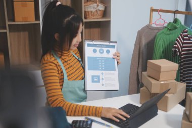 Vlogger, blog yazarı, küçük KOBİ iş kadını güzel bir kadın cep telefonuyla kıyafetleri satıyor canlı yayın satışı yapıyor, ana ofiste ürün sunumu detaylarını gösteriyor, girişimci ekommerce