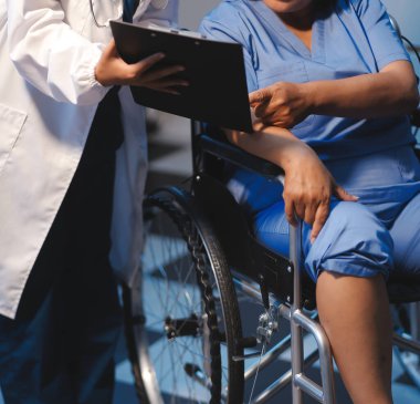 Asyalı, genç, profesyonel, dost canlısı mavi hastane üniformalı kadın hemşire yaşlı, yaşlı, sağlıksız, dört bacaklı, yürüyen bir hastanın fiziksel terapisine yardım ediyor..