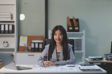 Ofiste dizüstü bilgisayarda çalışan neşeli iş kadını, iş yerinde resmi takım elbiseli Asyalı mutlu iş kadını. Çekici bayan ofis çalışanı gülümsemesi.