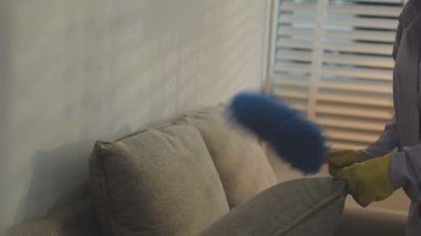 Kadın, odada bez parçasıyla kanepeyi temizliyor.