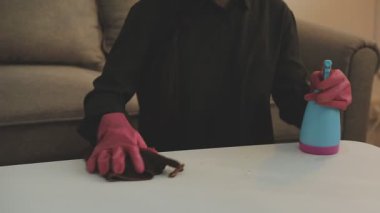 Siyah eldivenli kadın fırça ve spreyle masayı temizliyor.