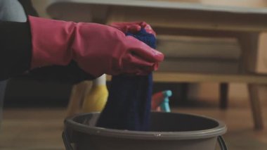 Lastik eldivenli bir kadın evi paçavrayla temizliyor.