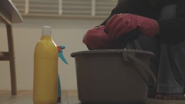 Sarı eldivenli kadın, evde kova mutfak zeminini temizliyor.
