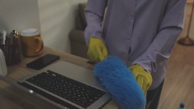 Masayı dizüstü bilgisayarla temizleyen mavi gömlekli genç hizmetçi.