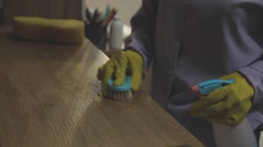 Bir kadının eli, ahşap zemini temizleyen sarı eldivenli.