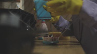 Yakın plan, mavi eldivenli bir kadının mutfağı temizlerken çekilmiş fotoğrafı. Üniformalı profesyonel bir işçi süngerle masaları temizliyor..