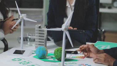 Asyalı işadamı rüzgar türbinli model bir rüzgar türbini tutuyor ve iş yerinde iki iş arkadaşı var.