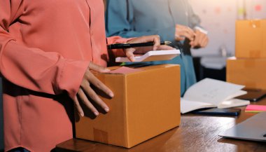 Girişim KOBİ küçük işletme girişimcisi önlük giyen Asyalı kadın dizüstü bilgisayar ve kutu kullanarak çevrimiçi müşterilere, çevrimiçi sme iş fikirlerine satış hazırlamak için siparişleri alır ve gözden geçirir.