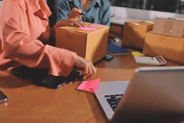 Girişim KOBİ küçük işletme girişimcisi önlük giyen Asyalı kadın dizüstü bilgisayar ve kutu kullanarak çevrimiçi müşterilere, çevrimiçi sme iş fikirlerine satış hazırlamak için siparişleri alır ve gözden geçirir.