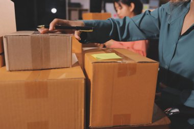 Girişim KOBİ küçük işletme girişimcisi önlük giyen Asyalı kadın dizüstü bilgisayar ve kutu kullanarak çevrimiçi müşterilere, çevrimiçi sme iş fikirlerine satış hazırlamak için siparişleri alır ve gözden geçirir.