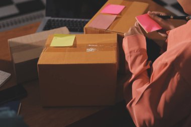 Girişim KOBİ küçük işletme girişimcisi önlük giyen Asyalı kadın dizüstü bilgisayar ve kutu kullanarak çevrimiçi müşterilere, çevrimiçi sme iş fikirlerine satış hazırlamak için siparişleri alır ve gözden geçirir.