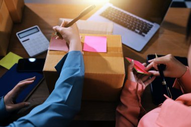 Girişim KOBİ küçük işletme girişimcisi önlük giyen Asyalı kadın dizüstü bilgisayar ve kutu kullanarak çevrimiçi müşterilere, çevrimiçi sme iş fikirlerine satış hazırlamak için siparişleri alır ve gözden geçirir.